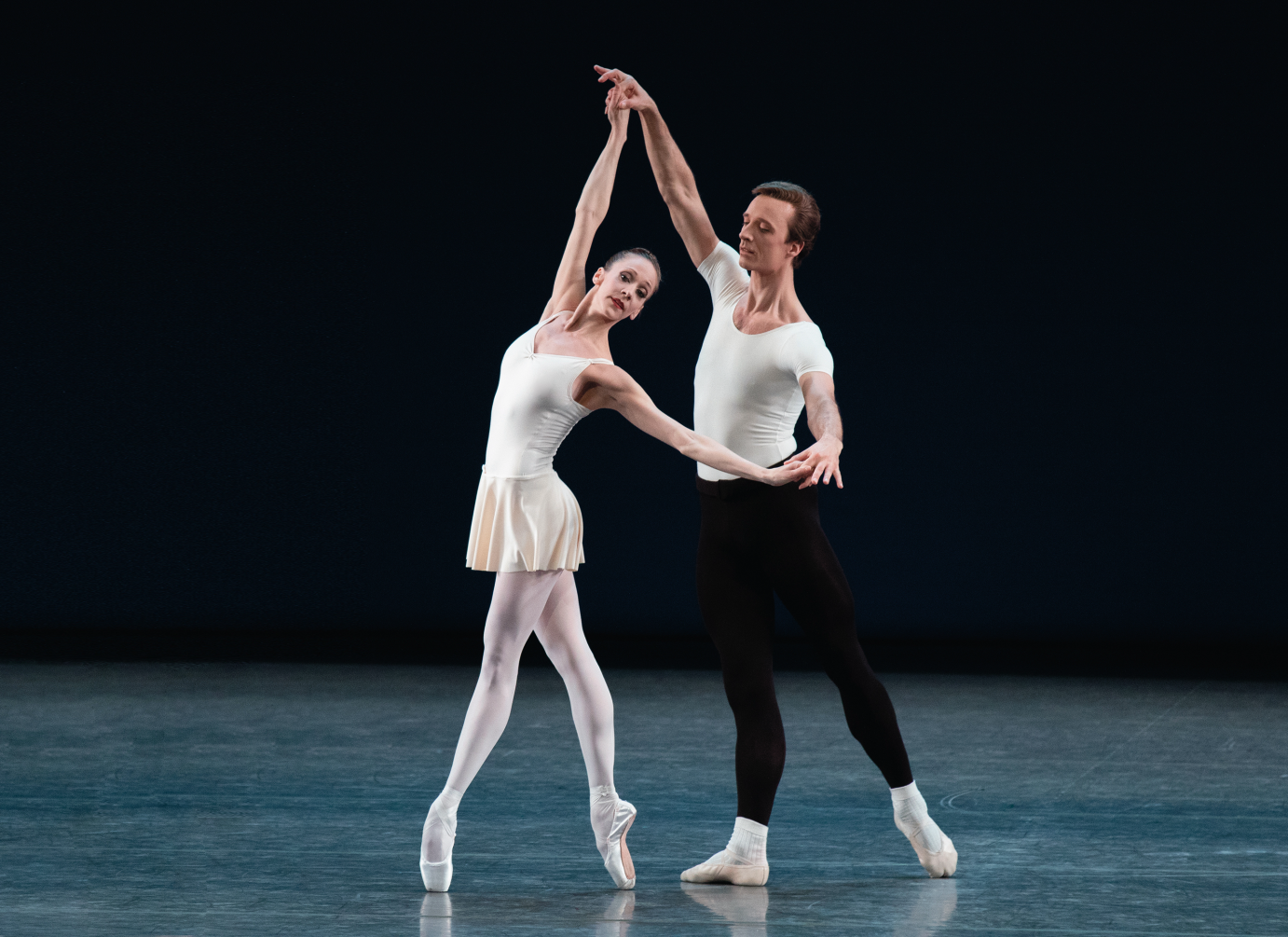 Ask la Cour stands in tendu derriere. He holds Maria Kowroski's hands. She is en pointe in fourth position.